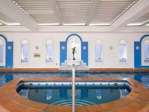 An indoor swimming pool with a tiled edge, a central fountain, and arched windows along the walls. - Broadbeach Holiday Apartments (Gold Coast)