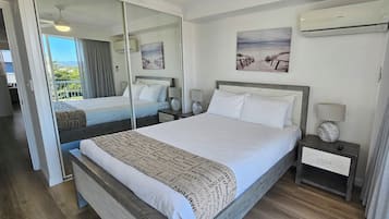 A hotel room with a large bed, two bedside tables, a mirror, and a view of the outdoors.