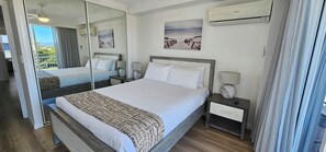 Quarto de hotel com uma cama grande, duas mesinhas de cabeceira, um espelho e vista para o exterior.
