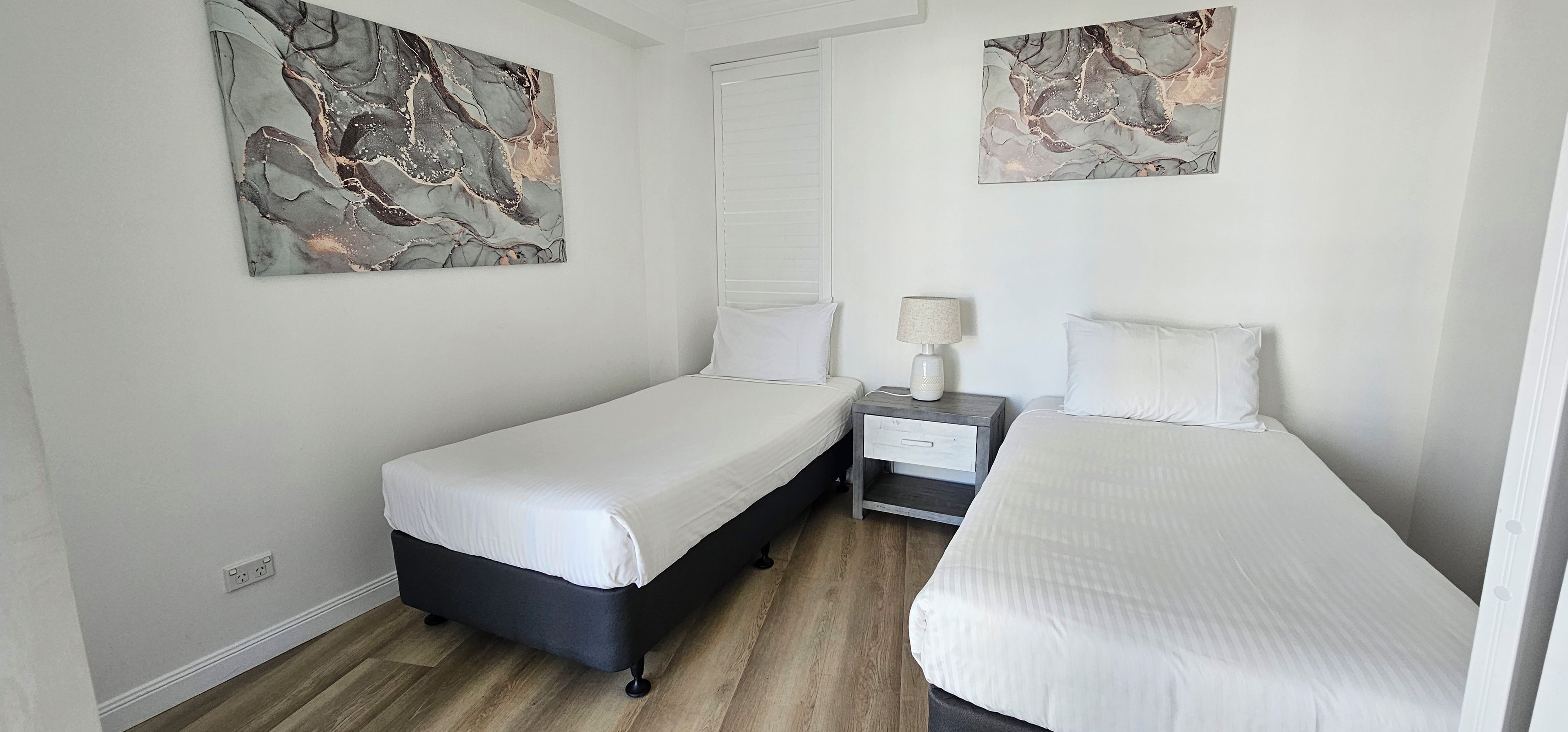 Una habitación de hotel con dos camas individuales, una mesita de noche con lámpara y arte abstracto en las paredes.