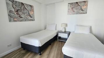 Una habitación de hotel con dos camas individuales, una mesita de noche con lámpara y arte abstracto en las paredes.