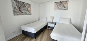 A hotel room with two single beds, a nightstand with a lamp, and abstract artwork on the walls. - Broadbeach Holiday Apartments (Gold Coast)