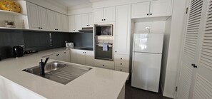 A modern kitchen with white cabinets, stainless steel appliances, and a black countertop. - Broadbeach Holiday Apartments (Gold Coast)