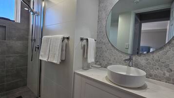 A modern bathroom with a glass-enclosed shower, a round mirror, and a white sink.