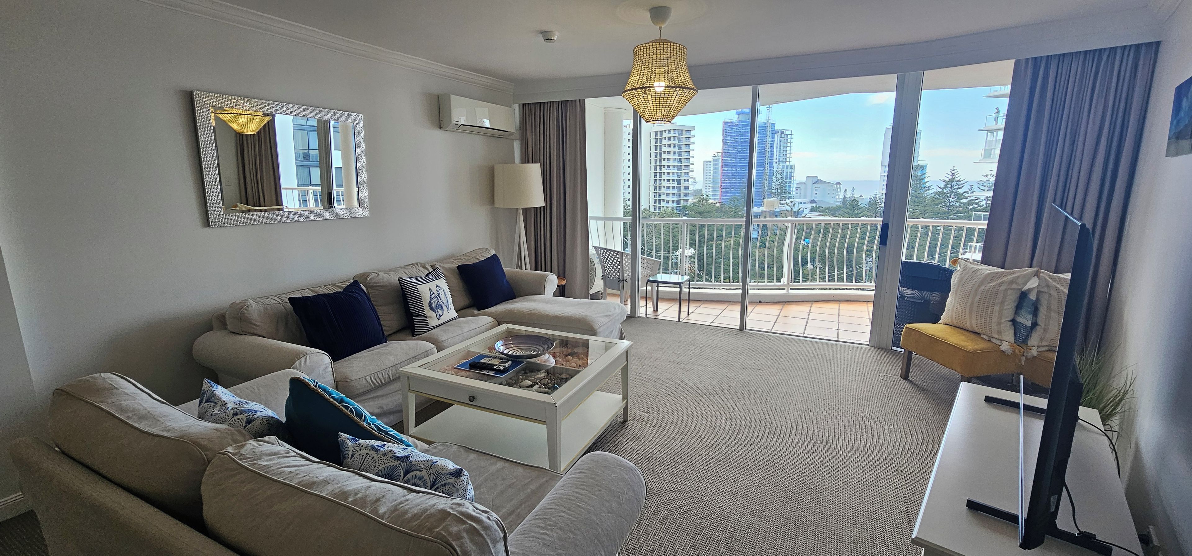 A modern living room with a sofa set, a coffee table, and a large window offering a city view.