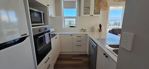 A compact kitchen with white cabinetry, a built-in microwave, oven, and dishwasher. There is a window providing natural light and a view of the outside. - Broadbeach Holiday Apartments (Gold Coast)