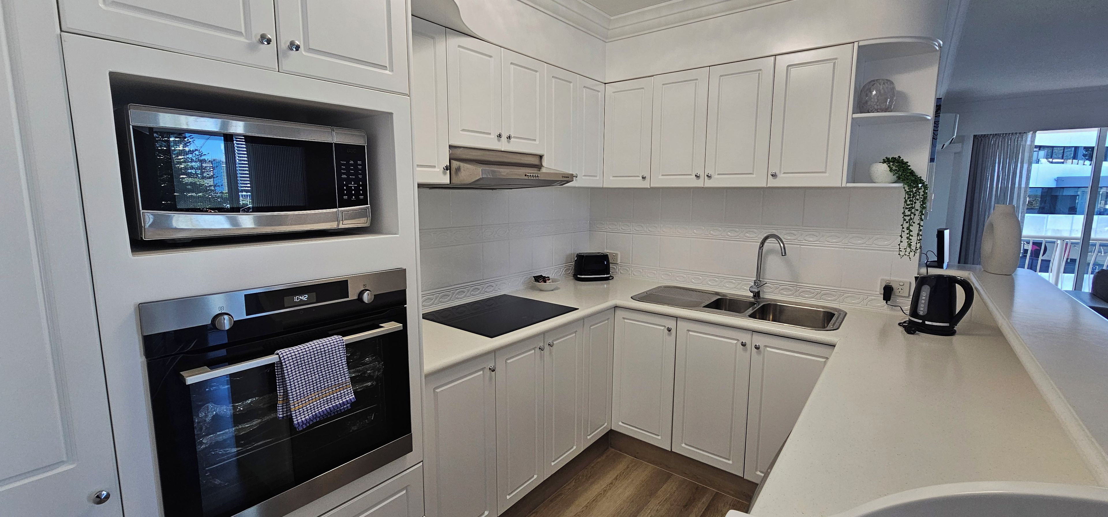 A modern kitchen with white cabinetry, a built-in microwave, a stove, and a sink.
