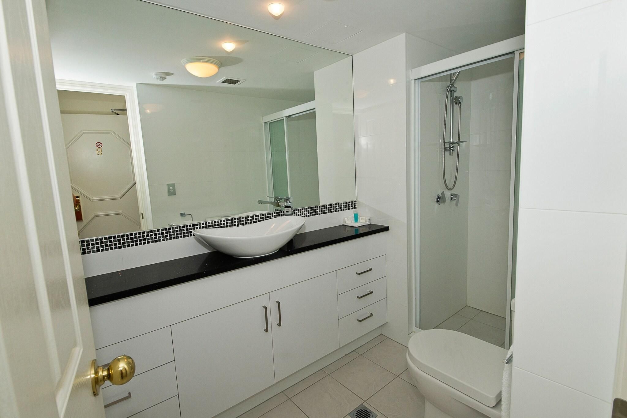 A bathroom with a white sink, black countertop, and a glass shower enclosure.