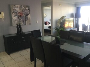 Uma sala de jantar moderna com mesa de vidro, cadeiras pretas, um vaso com flores e um quadro na parede.