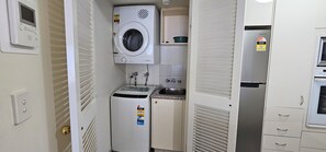 A compact laundry room with a washing machine, a dryer, a sink, and a refrigerator. - Broadbeach Holiday Apartments (Gold Coast)