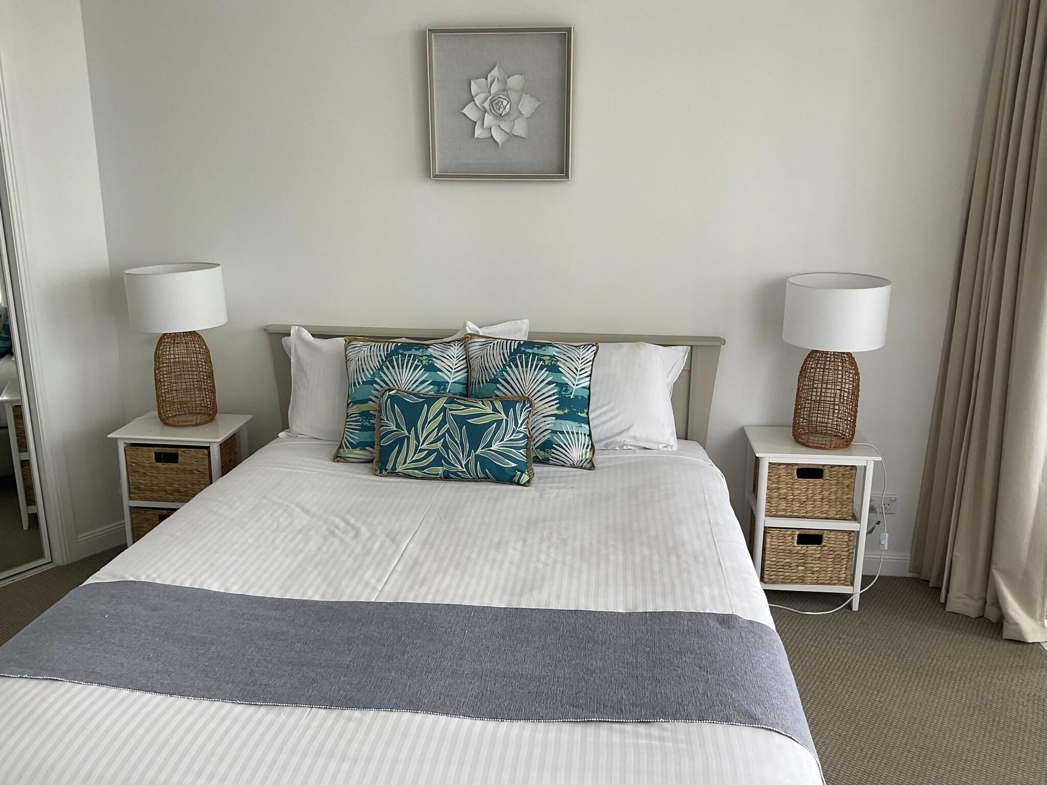 A neatly made bed with a striped blanket, two bedside tables with lamps, and a wall-mounted picture.