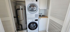 A compact laundry room with a stacked washer and dryer, a water heater, and a small sink. - Broadbeach Holiday Apartments (Gold Coast)