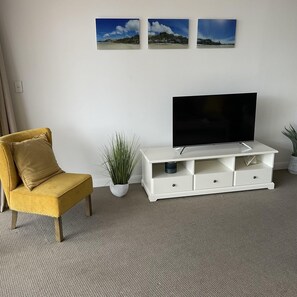 A living room with a yellow armchair, a white entertainment unit with a TV, and three framed pictures on the wall. - Broadbeach Holiday Apartments (Gold Coast)