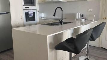 A modern kitchen with a central island, stainless steel appliances, and two bar stools.