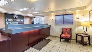 A reception area with a reception desk, a chair, a lamp, and a sign for HomeTOWNE Studios. - Sun Suites of Louisville (Louisville)