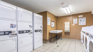 A laundromat with multiple washing machines and dryers, a small sink, and instructional posters on the walls. - Sun Suites of Louisville (Louisville)