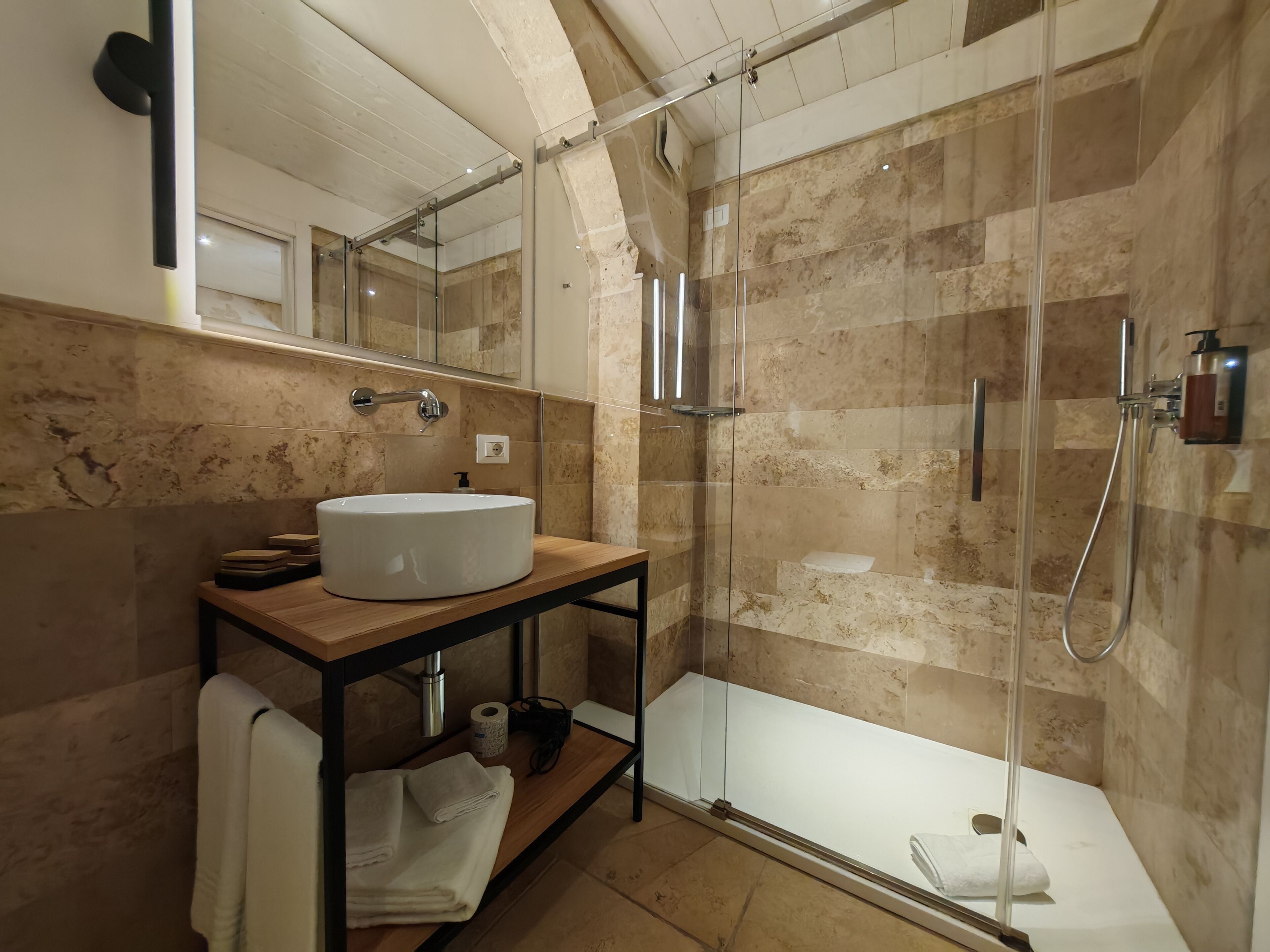 A modern bathroom with a glass-enclosed shower, a wooden vanity with a sink, and a mirror.