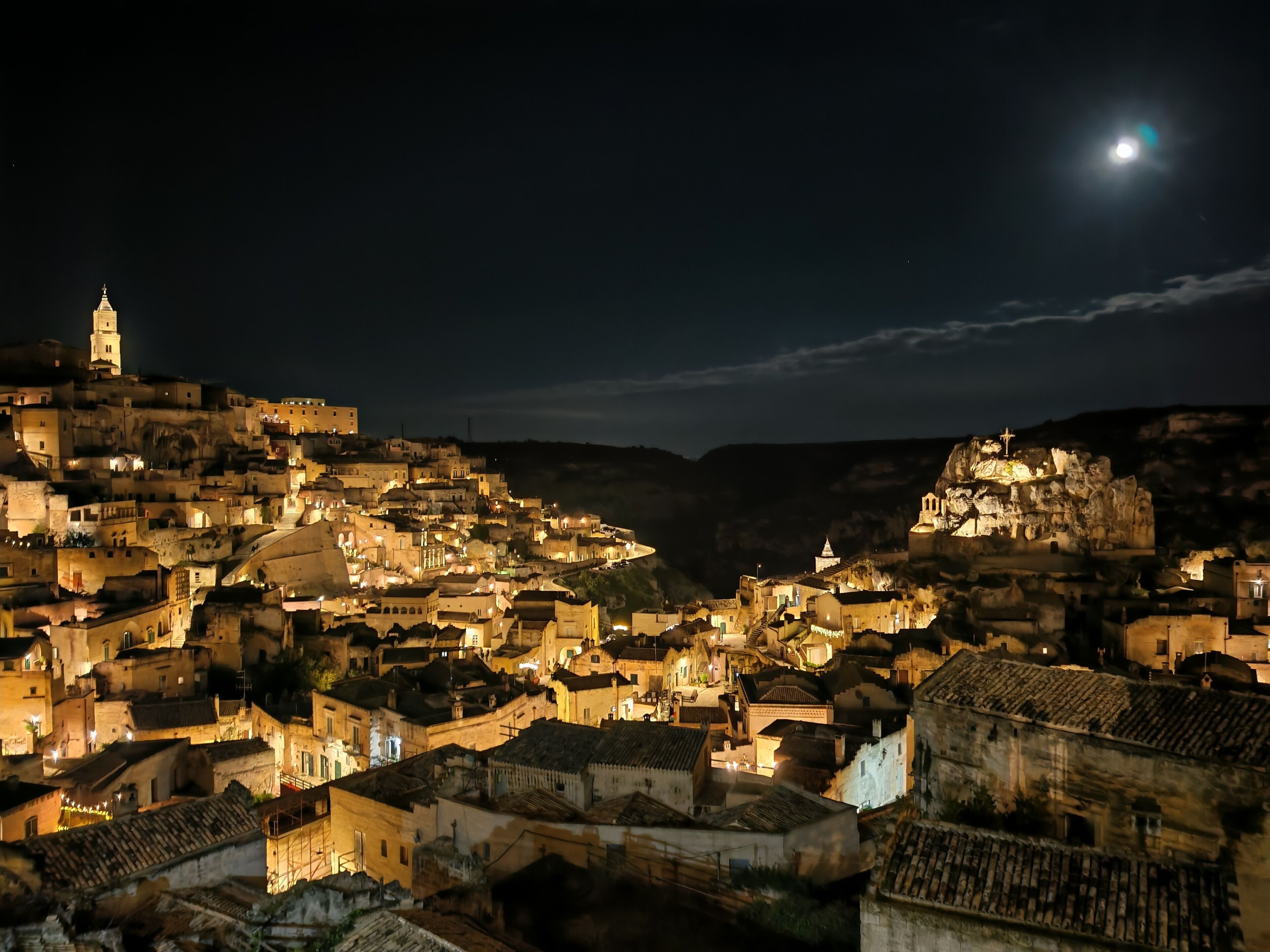 Un poble històric de nit, amb edificis il·luminats i una església destacada en un turó.