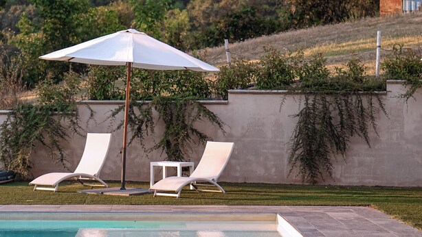 A swimming pool with lounge chairs and an umbrella, surrounded by a landscaped garden and a hillside.