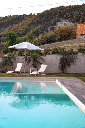 A swimming pool with lounge chairs and an umbrella, surrounded by a landscaped garden and a hillside. - Cozy house in the hills of Parma, with garden and a beautiful pool (Solignano)
