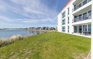 A modern building with large windows, a grassy area, and a view of the water and other buildings. - Stunning apartment in Kappeln with sauna (Kappeln)