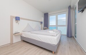 Ein modernes Hotelzimmer mit Bett, Nachttischen, einem Fenster mit Blick und einem Balkon.