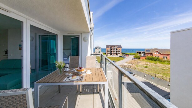 Een balkon met een eettafel, uitzicht op zee en een woongebied op de achtergrond.