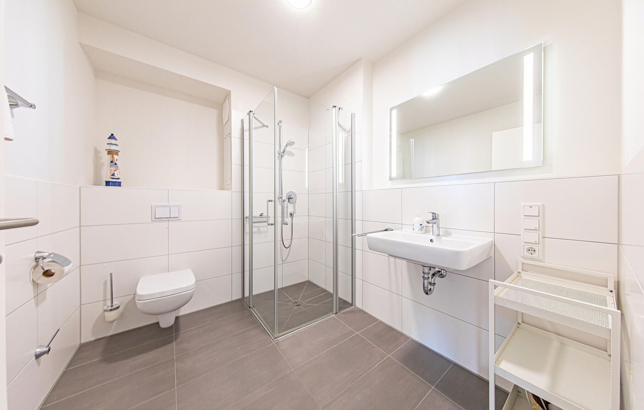 Un baño moderno con inodoro, ducha y lavabo, que cuenta con un box de ducha de vidrio y un espejo grande sobre el lavabo.