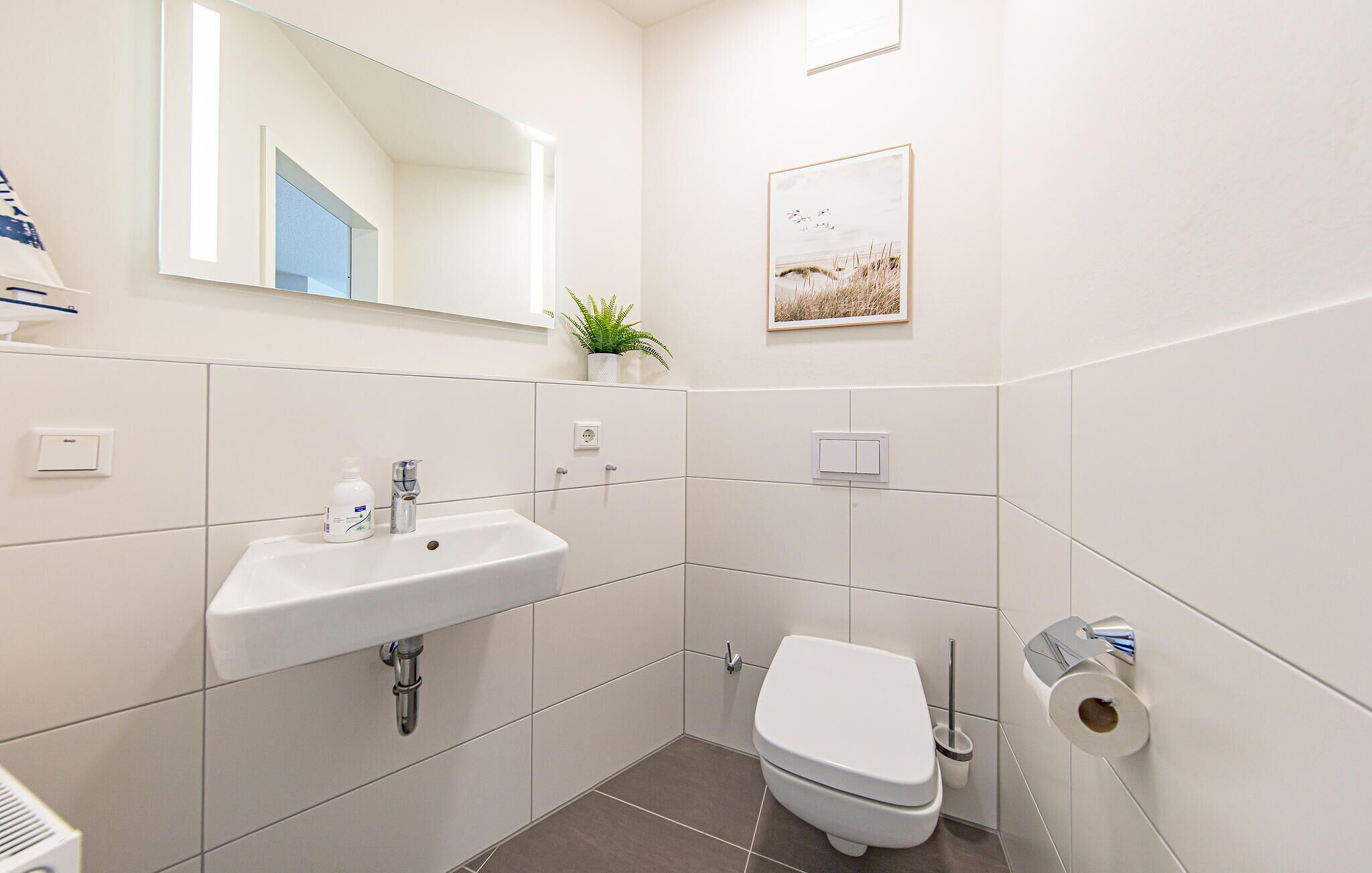 A modern bathroom with a white sink, toilet, and a mirror above the sink.