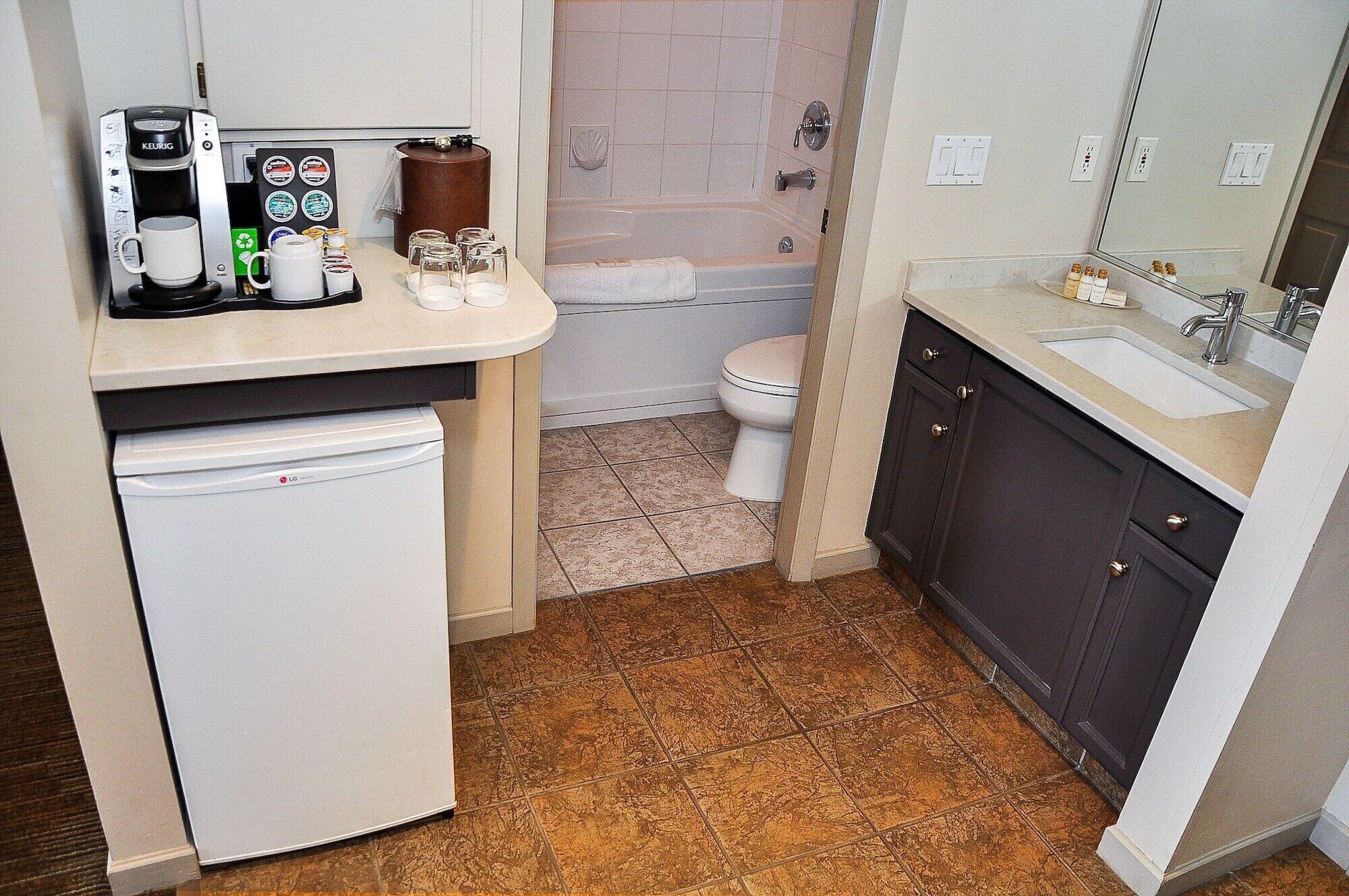 A compact bathroom with a coffee maker, a toilet, a sink, and a mirror.