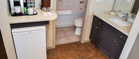 A compact bathroom with a coffee maker, a toilet, a sink, and a mirror.