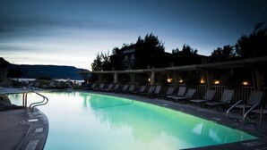 Una piscina con sillas de descanso y una zona cubierta, rodeada de árboles y una montaña al fondo.