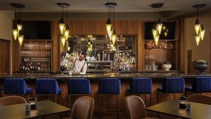 Un área de bar con paneles de madera, taburetes azules y lámparas colgantes.