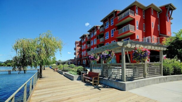 Una terraza de madera con un banco, un pabellón floral y un edificio rojo con balcones.