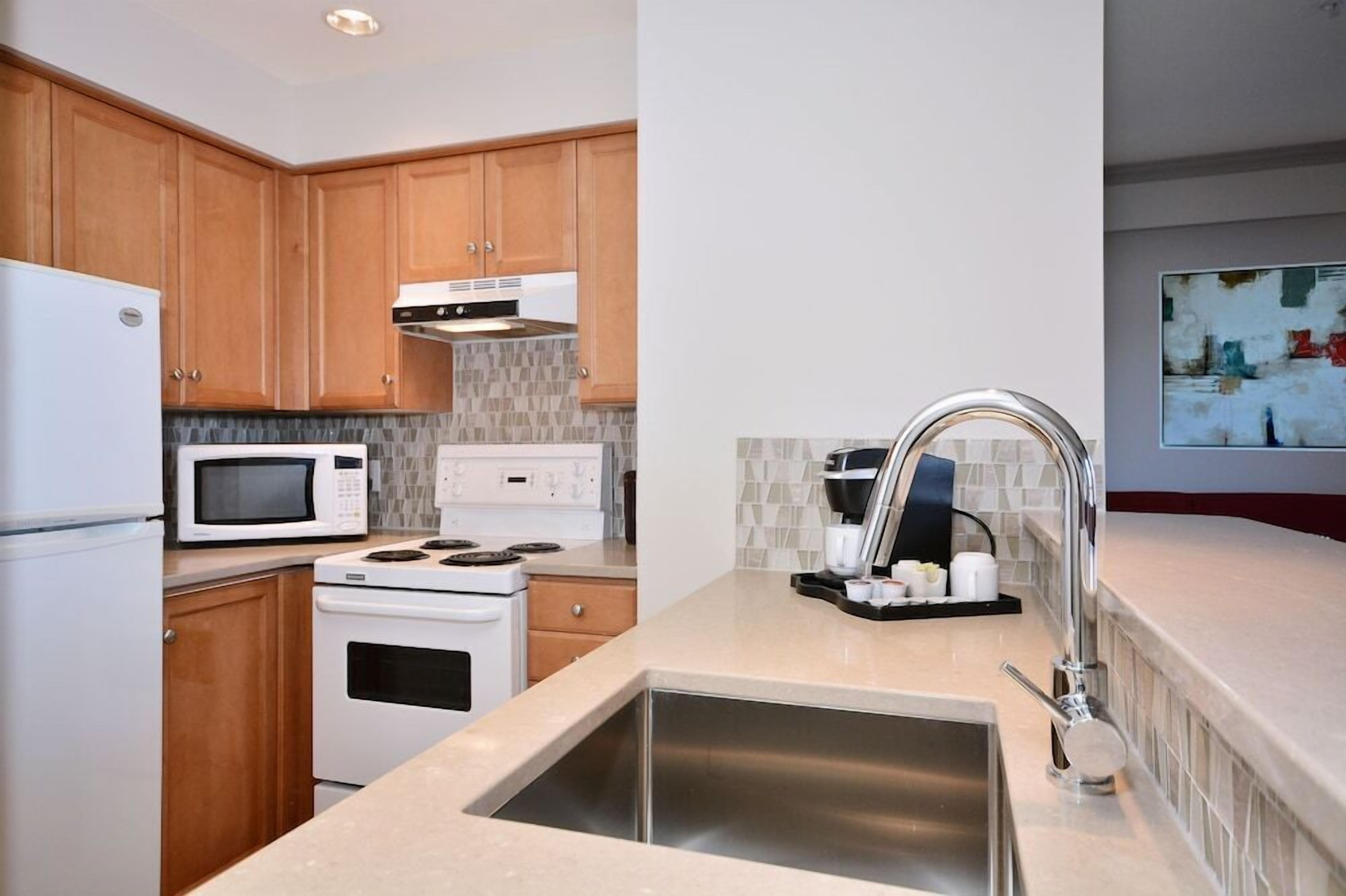 A modern kitchen with wooden cabinets, a stainless steel sink, a microwave, a stove, and a coffee maker.
