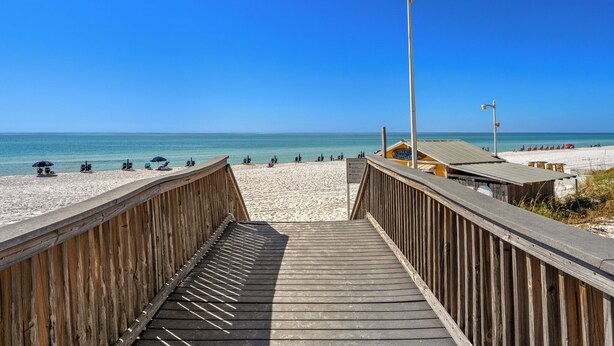Une promenade en bois mène à une plage, avec un ciel bleu dégagé.