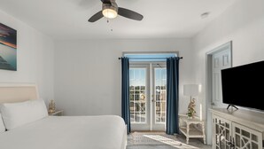 Et soveværelse med seng, ventilator, fjernsyn, skab og udsigt til det fri gennem en glasdør.
