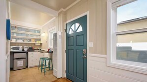 A compact kitchen with white cabinets, a teal door, and a window. - Bayfront Studio, Walk to Beach & Shops | Edgewater (Newport Beach)