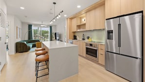 A modern kitchen with a central island, stainless steel appliances, wooden cabinets, and a seating area with a sofa and bar stools.