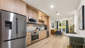 A modern kitchen with stainless steel appliances, wooden cabinets, and a dining area with a table and chairs. - Pool + Rooftop | 1BDR Suite w/ Balcony | The Code (Austin)