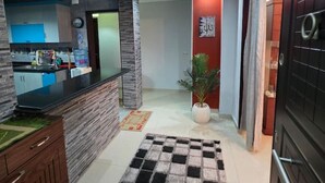 A modern kitchen with a black countertop and wooden cabinets, a hallway with a checkered rug, and a potted plant. - Executive Exclusive Cairo Mohandessin Giza Apart. (Gazirat Mit Oqbah)