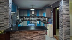 A modern kitchen with a central island, blue cabinets, and a unique ceiling light fixture. - Executive Exclusive Cairo Mohandessin Giza Apart. (Gazirat Mit Oqbah)