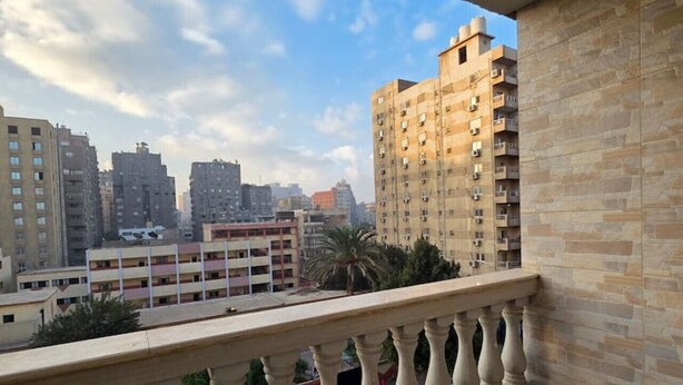 A balcony with a view of a cityscape, including high-rise buildings and a palm tree. - Executive Exclusive Cairo Mohandessin Giza Apart. (Gazirat Mit Oqbah)