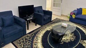 Olohuoneessa on kaksi sinistä nojatuolia, musta sohva, lasinen sohvapöytä ja musta mediakeskus.