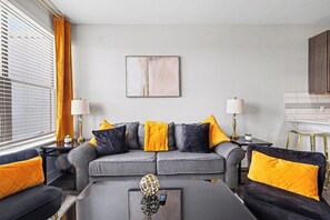 Ein modernes Wohnzimmer mit einem grauen Sofa, gelben Kissen, einem schwarzen Couchtisch und einem Bild an der Wand.