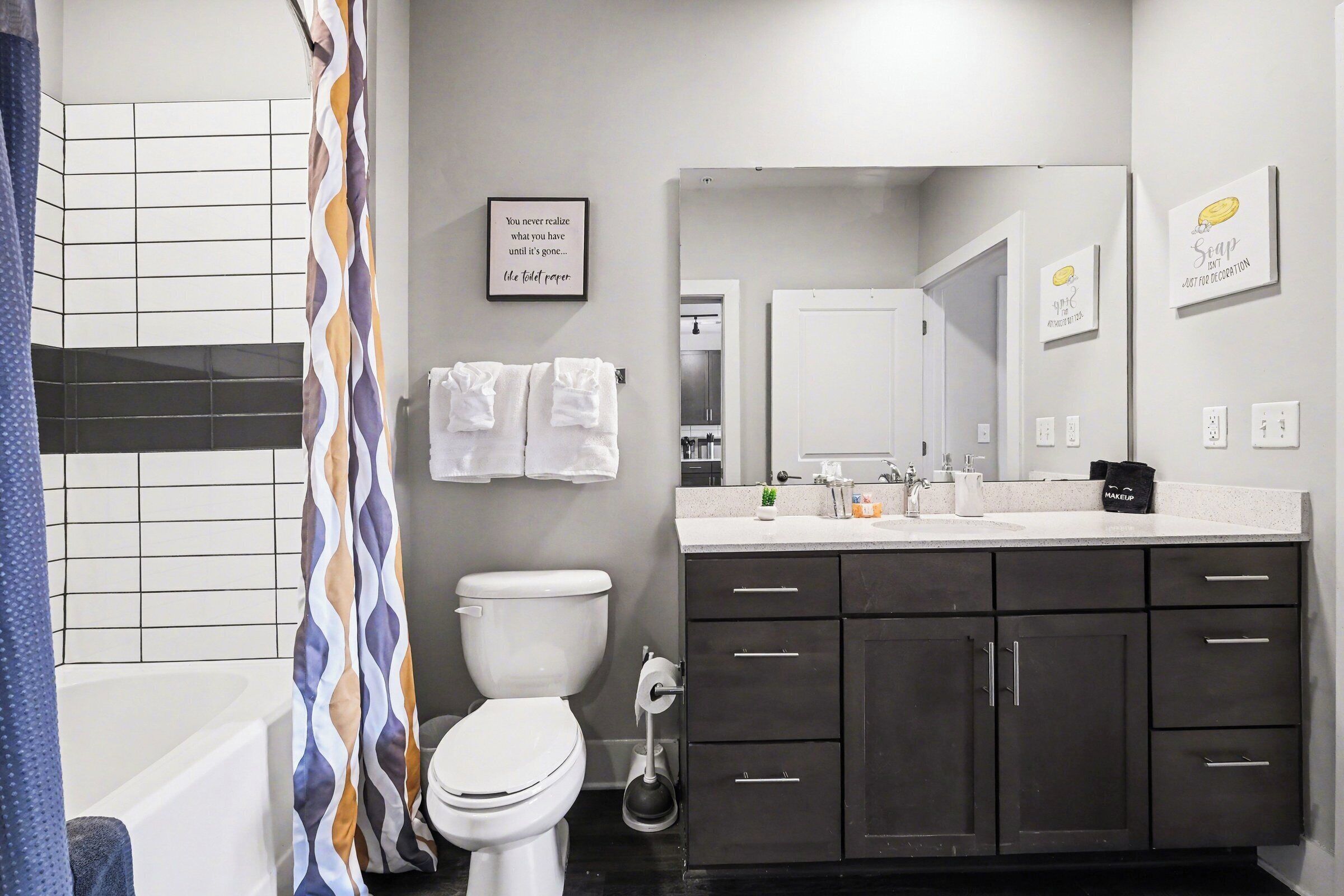 Une salle de bain moderne équipée de toilettes, d’un lavabo et d’une douche. Des serviettes sont accrochées au mur et un distributeur de savon est posé sur le comptoir.