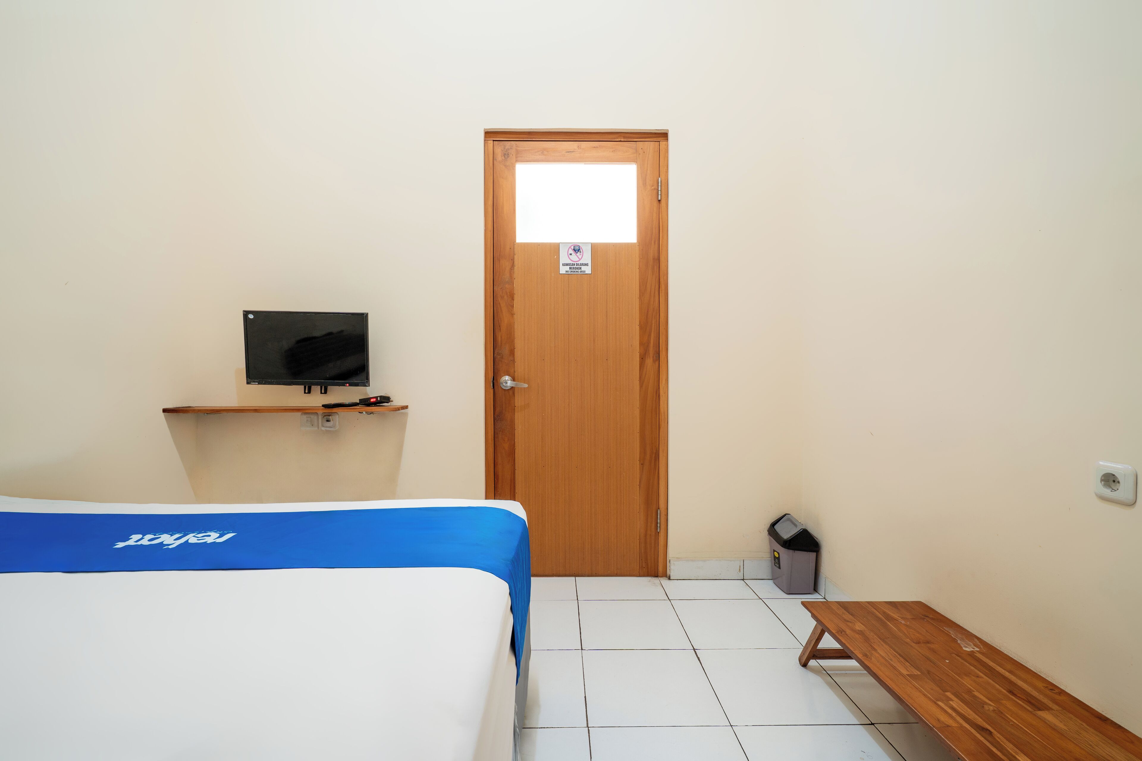 A room with a bed, a bench, a television on a stand, and a door.