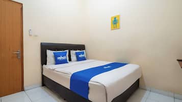 Een net opgemaakt bed met een blauw-witte sprei, twee kussens met 'rehat'-logo en een klein kunstwerk aan de muur.