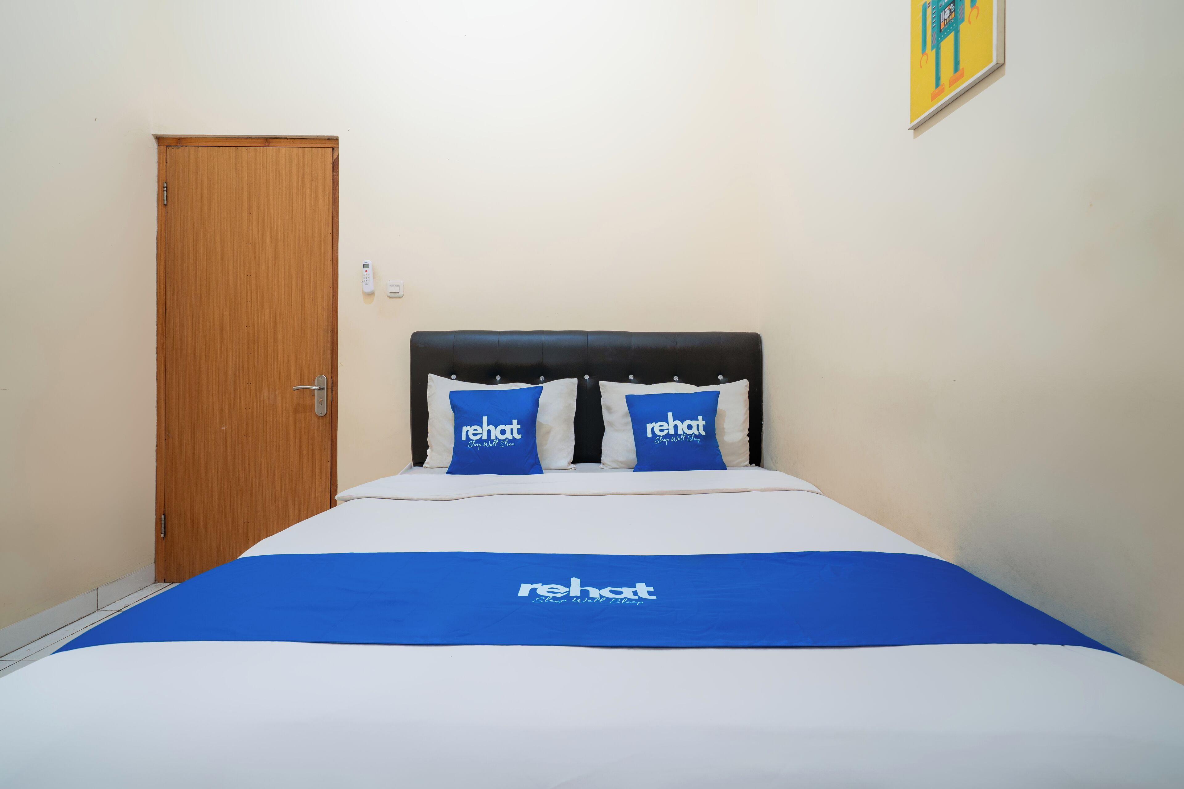 A hotel room with a bed, a wooden door, and a wall-mounted light switch.