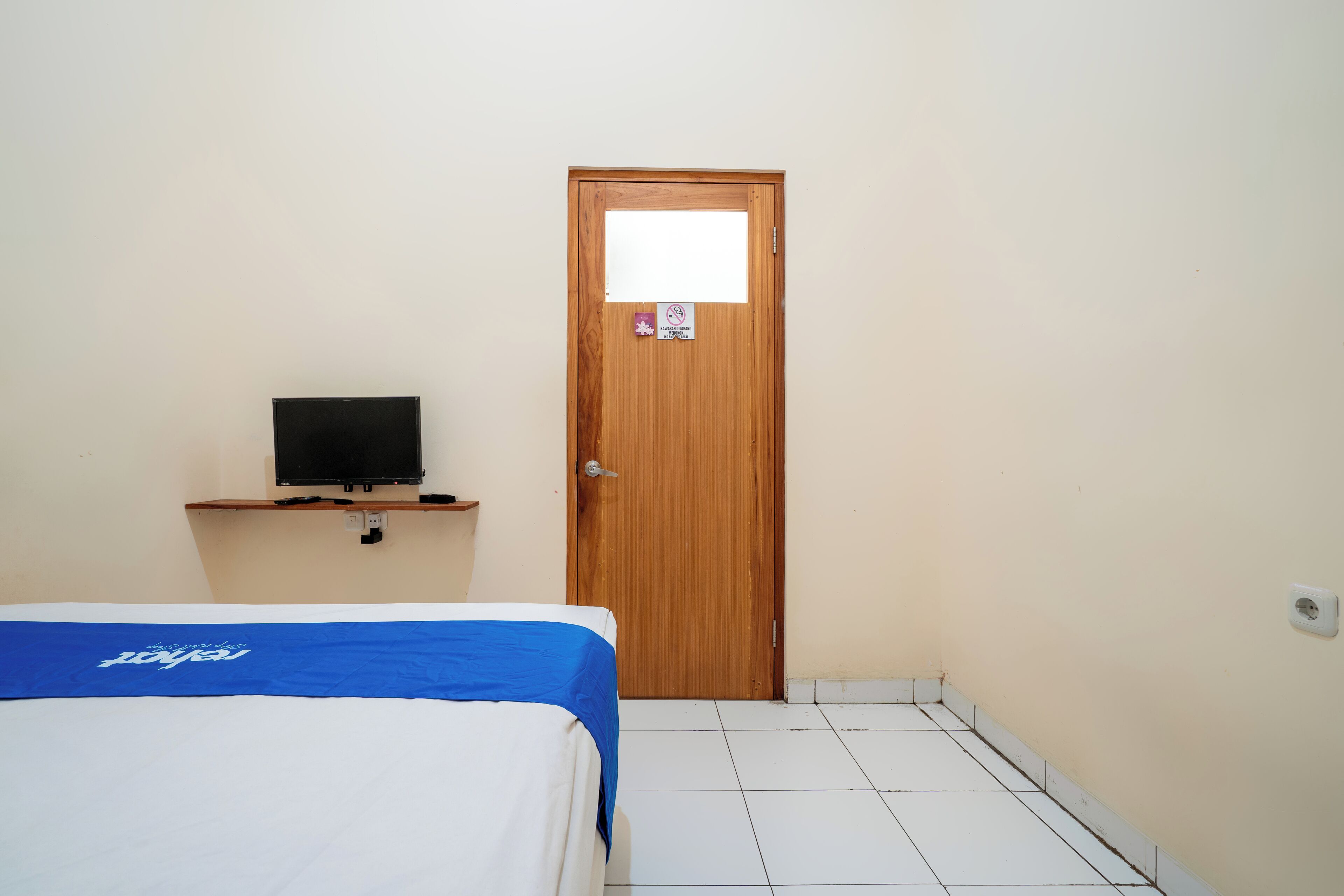 Una habitación con una cama, un televisor en un estante y una puerta con un letrero.